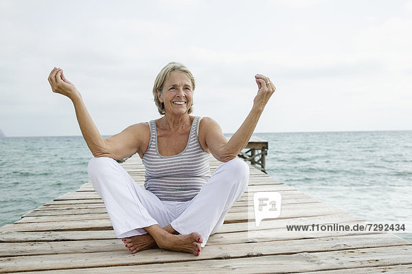 Spain  Senior woman doing yoga on jetty at the sea