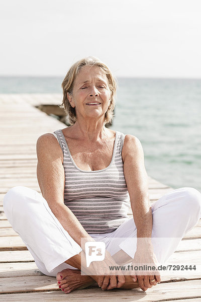 Spanien  Seniorin beim Yoga am Steg am Meer