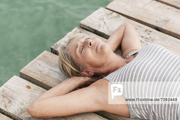 Spain,  Senior woman relaxing on jetty at the sea