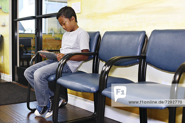 Mixed race boy using digital tablet in waiting room
