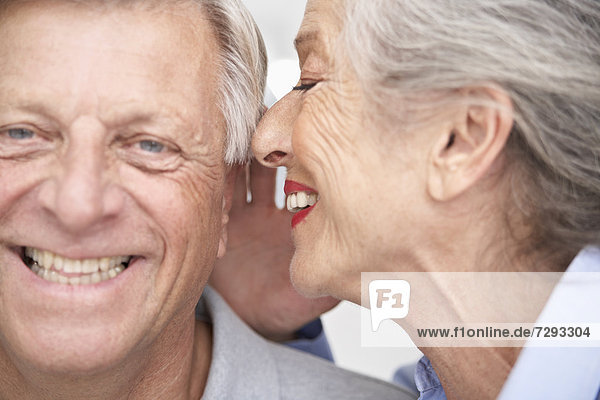 Spain  Senior woman whispering into ear of man  smiling