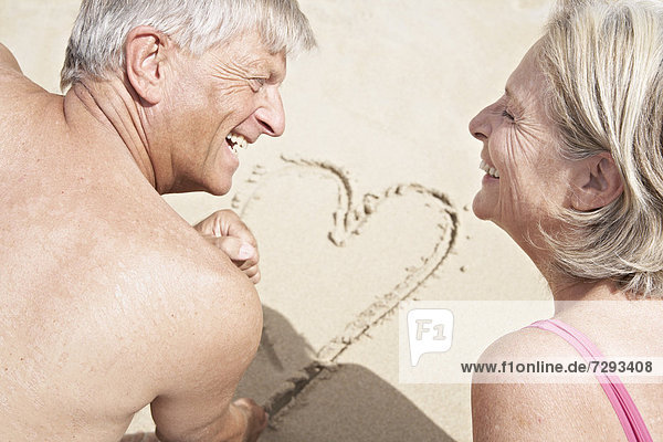Spain  Senior couple on beach drawing heart in sand  smiling