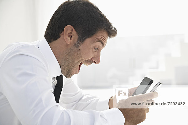 Spain  Businessman confused of using two mobile phone  smiling