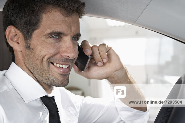 Spain  Businessman sitting in car and talking on mobile phone  smiling