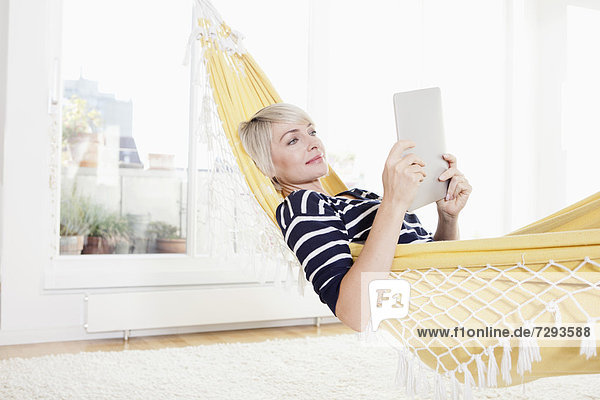 Woman relaxing in hammock and watching digital tablet
