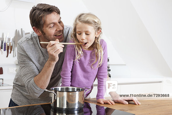 Germany  Bavaria  Munich  Father feeding daughter in kitchen  smiling