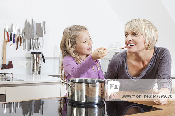 Germany  Bavaria  Munich  Daughter feeding mother in kitchen  smiling