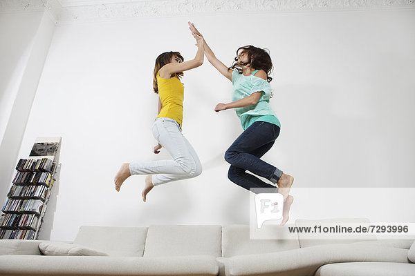 Young women having fun and jumping on couch