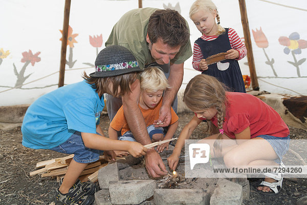 Germany  Munich  Father with children preparing camp fire in tent