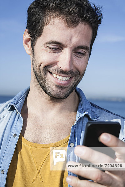 Spain  Mid adult man using smart phone  smiling