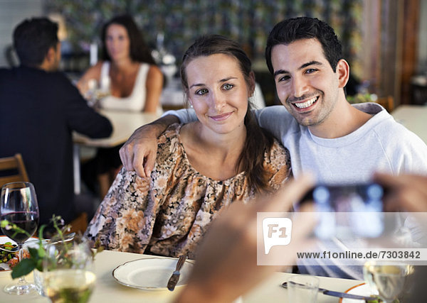 Glückliche junge Freunde  die am Restauranttisch mit Menschen im Hintergrund fotografieren.