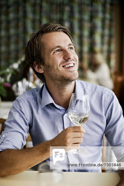 Happy young man holding wine glass at restaurant table while looking up