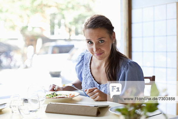 Porträt einer jungen Frau beim Essen mit dem digitalen Tablett am Restauranttisch