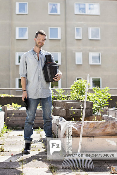 Porträt eines jungen Mannes mit gestapelten Blumentöpfen im Stadtgarten