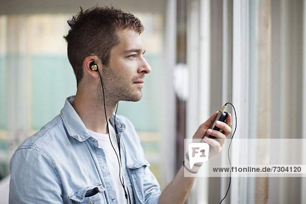 Side view of thoughtful young man listening music through cell phone