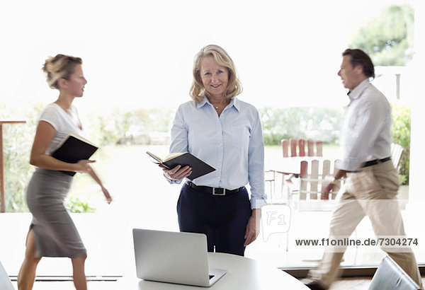 Portrait of senior businesswoman standing with colleagues walking behind at office