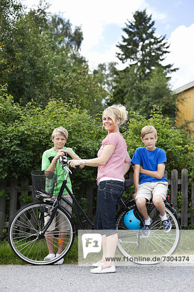 Porträt einer glücklichen reifen Frau mit Söhnen  die mit dem Fahrrad auf der Straße stehen.