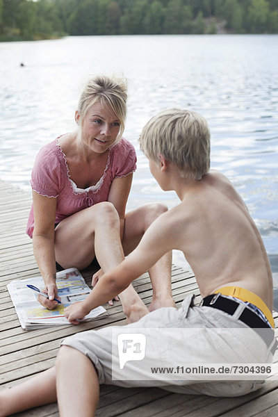 Reife Frau  die auf Zeitungen schreibt  während sie mit ihrem Sohn auf dem Pier redet