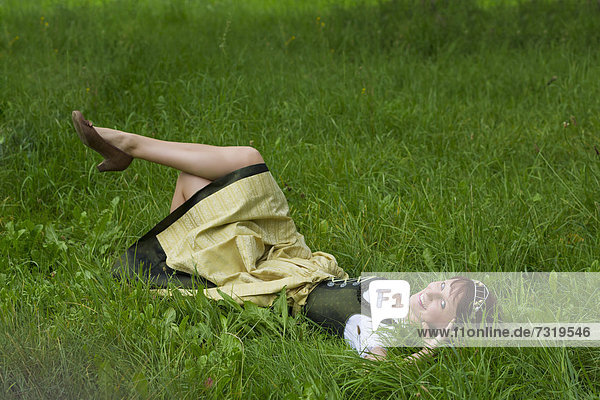 Junge Frau im Dirndl und mit Hopfenkrone liegt im Gras  Hopfenvizekönigin der Hallertau  Holledau oder Hollerdau  Bayern  Deutschland  Europa