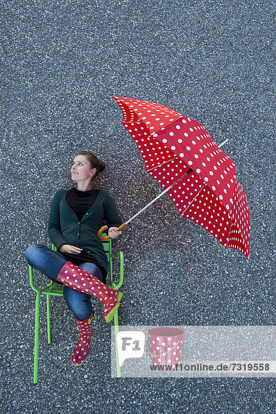 Junge Frau scheint mit einem gepunkteten Regenschirm auf einem Stuhl zu sitzen  von oben aufgenommen