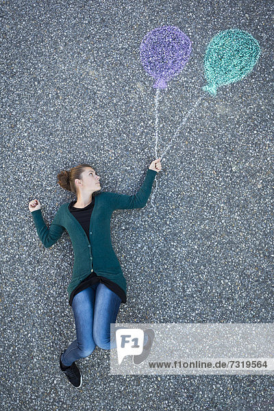 Junge Frau scheint an zwei gemalten Luftballons zu hängen  von oben aufgenommen