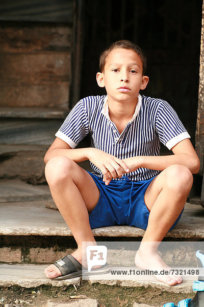 Junge mit nur einer Sandale sitzt in einem Hinterhof  Havanna  Kuba