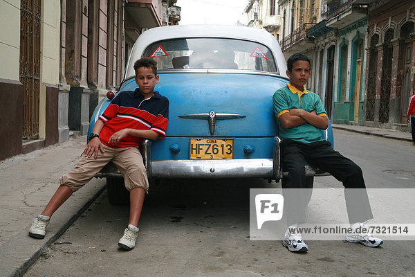 Two boys casually leaning against a vintage car with a couple making out in the back seat  Havana  Cuba  Caribbean  Americas