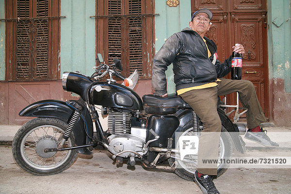 An elderly man sitting on his vintage motorcycle holding a bottle of Cuban cola (tu cola)  Havana  Cuba  Caribbean  Americas