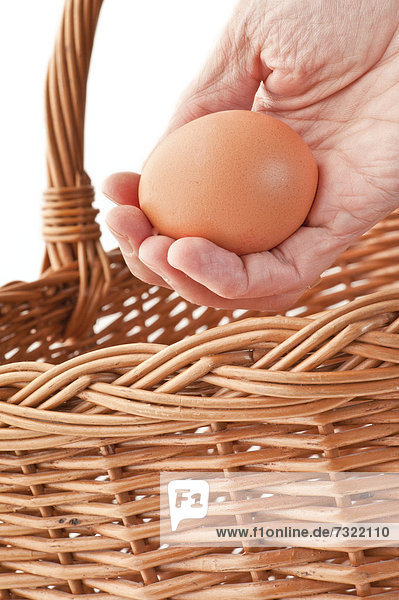 Hand placing a brown egg in a basket