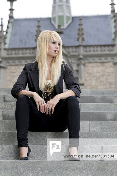 Junge Frau mit langen blonden Haaren posiert auf Steintreppe