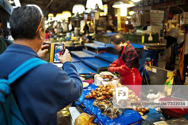 Mann benutzt ein Smartphone um ein Foto auf dem Noryangijn Fischmarkt in Seoul zu schießen  Südkorea  Asien