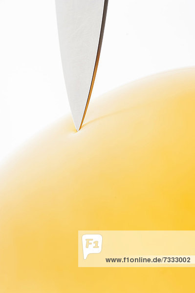 Scharfe Messerspitze auf einem gelben Luftballon
