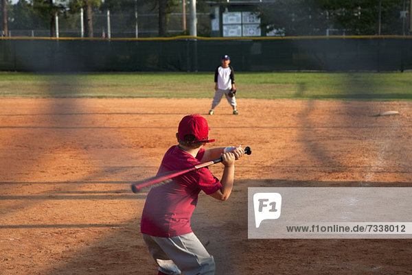 Rückansicht eines Jungen  der sich darauf vorbereitet  einen Schläger auf einem Baseball-Diamanten zu schwingen.