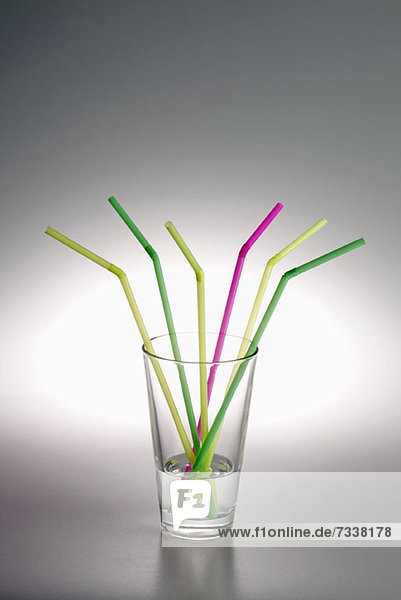 Ein Glas mit Wasser und drei gelbe Trinkhalme,  zwei grüne und ein rosa.