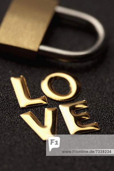 Einzelwort'Liebe' in goldener Schrift neben Vorhängeschloss