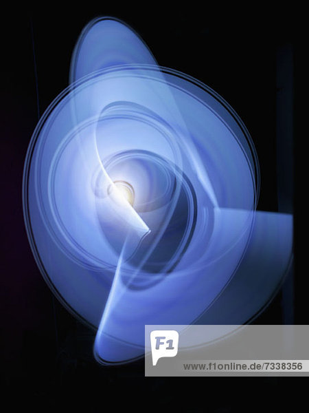 Lichtspuren  die ein abstraktes blaues  wirbelndes Kreismuster auf schwarzem Hintergrund erzeugen.