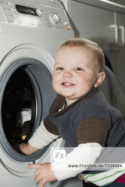 Ein kleiner Junge steht neben einer Waschmaschine.