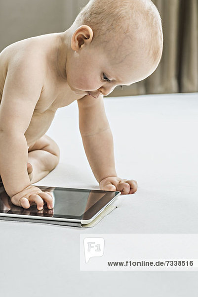 Baby betrachtet digitales Tablett auf dem Bett