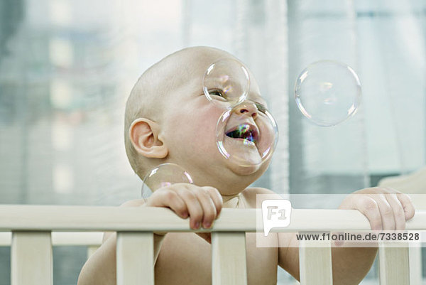 Baby im Kinderbett genießt die Blasen