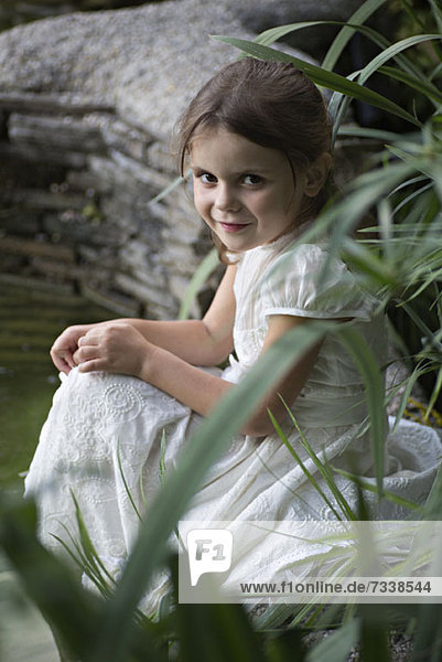 Ein junges Mädchen in einem weißen Kleid sitzt in der Natur.