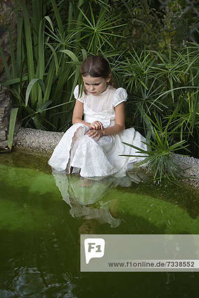 Ein junges Mädchen schaut neugierig ins Teichwasser.