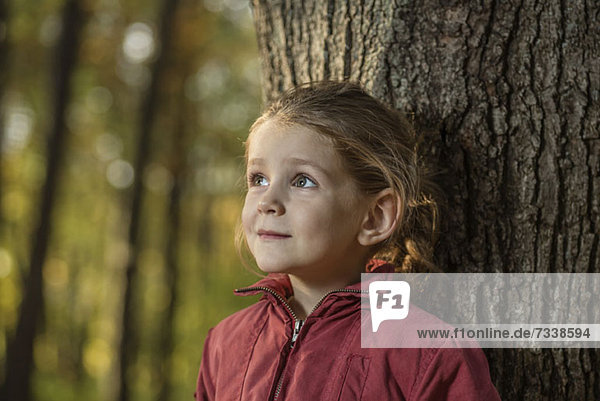 Ein junges Mädchen  das sich an einen Baumstamm lehnt.