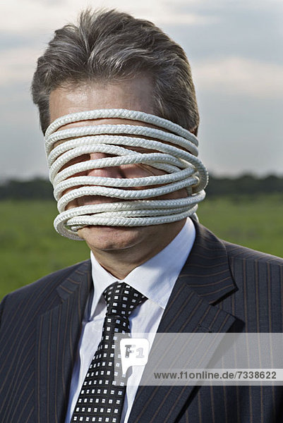 A mature businessman with rope wrapped around his face