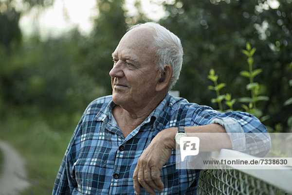 A senior man leaning on a fence and looking away serenely