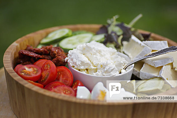 A wooden salad bowl filled with various vegetables and cheeses