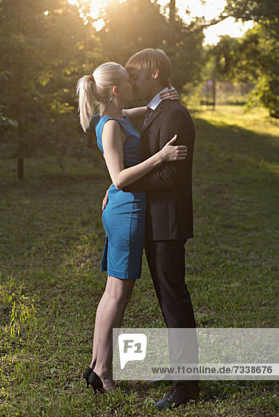 Ein gut gekleidetes Paar  das sich in einem Park umarmt und küsst.