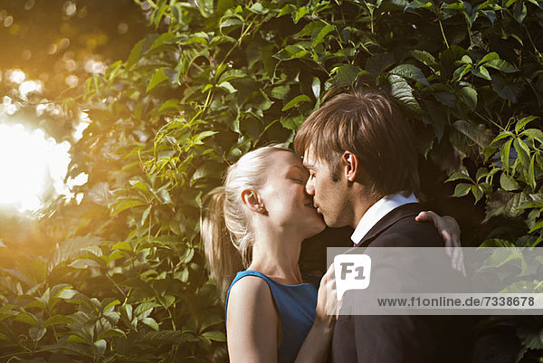 A well-dressed couple kissing in a park