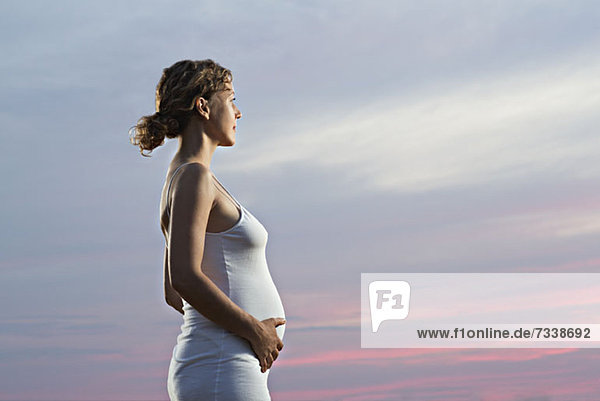 A pregnant woman holding her belly and looking away at a dramatic sky