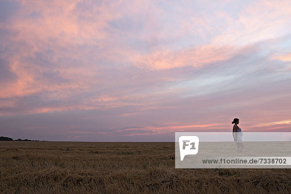 Eine schwangere Frau steht in einem abgelegenen Feld unter einem dramatischen Himmel.