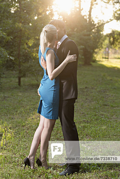 An elegantly dressed man kissing his girlfriend passionately while squeezing her bottom